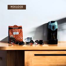 Mokador coffee packaging and coffee machine on a wooden surface with a white background