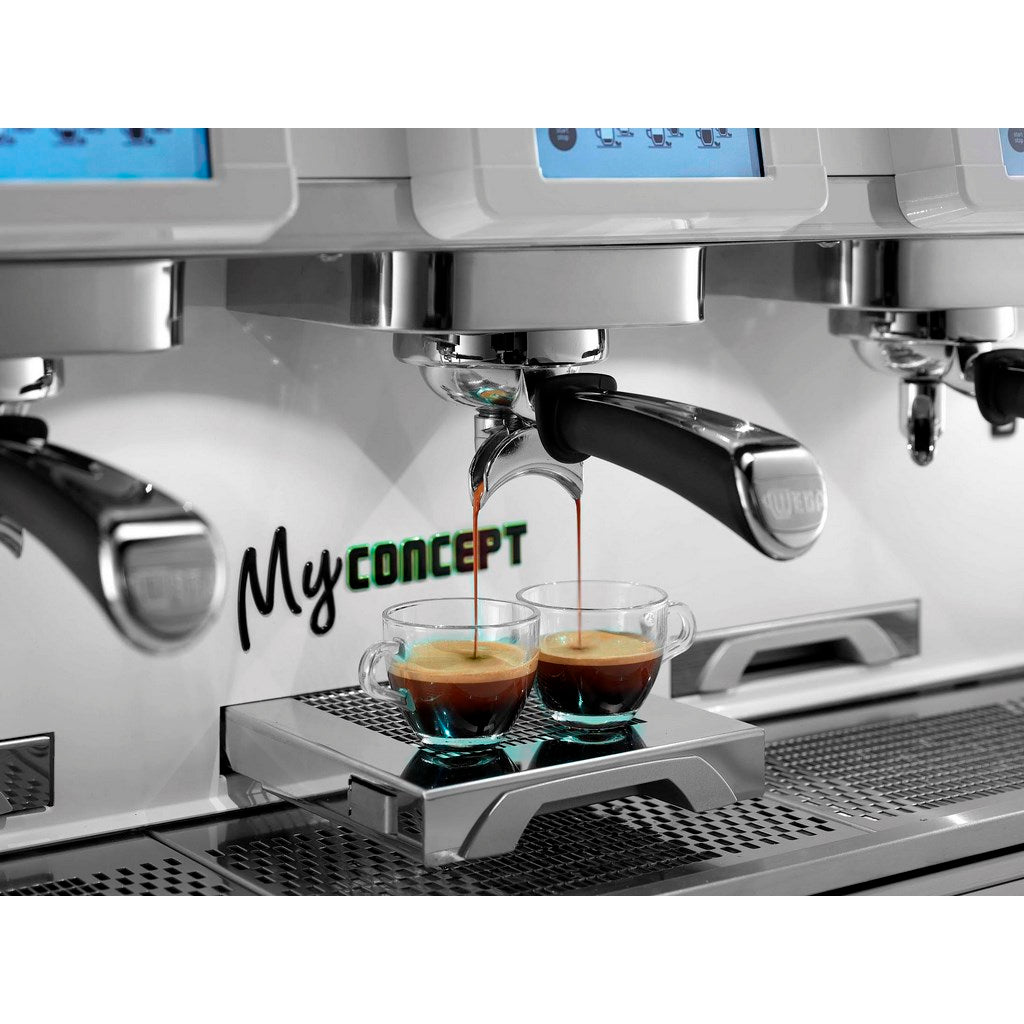A close-up of a commercial espresso machine dispensing two shots of espresso into small clear cups on a drip tray. The machine has a metallic silver and white finish with digital control panels, and the text 'MyCONCEPT' Fzin Coffee Ireland