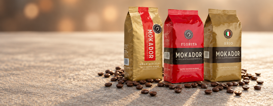 Three bags of Mokador coffee beans arranged on a stone surface with scattered coffee beans, set against a warm, blurred bokeh background. The bags are gold, red Fzin Coffee Ireland